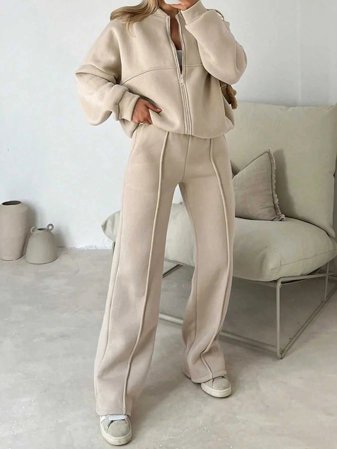 Person wearing a beige tracksuit in a minimalistic room with a white wall and light-colored furniture.