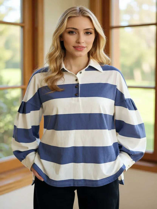 Woman wearing a blue and white striped shirt standing in a room with large windows.