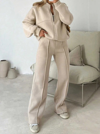 Person wearing a beige tracksuit in a minimalistic room with a white wall and light-colored furniture.